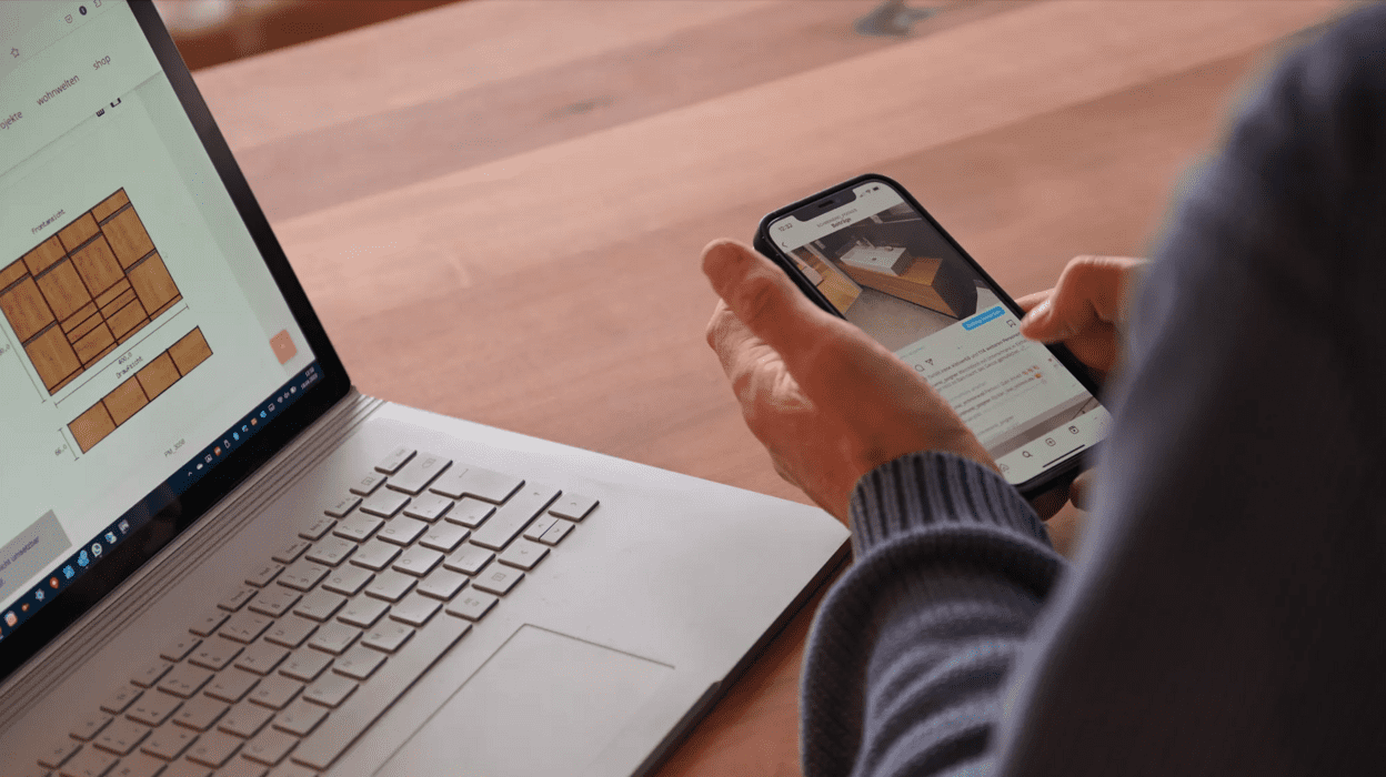 Mobile- und Desktopansicht Person, die Handy in der Hand hält neben Desktop, auf dem Möbelplanung geöffnet ist